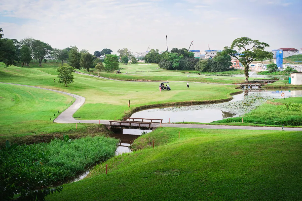 A scenic view of a lush green golf course featuring a small bridge over a winding water hazard and a cart path.