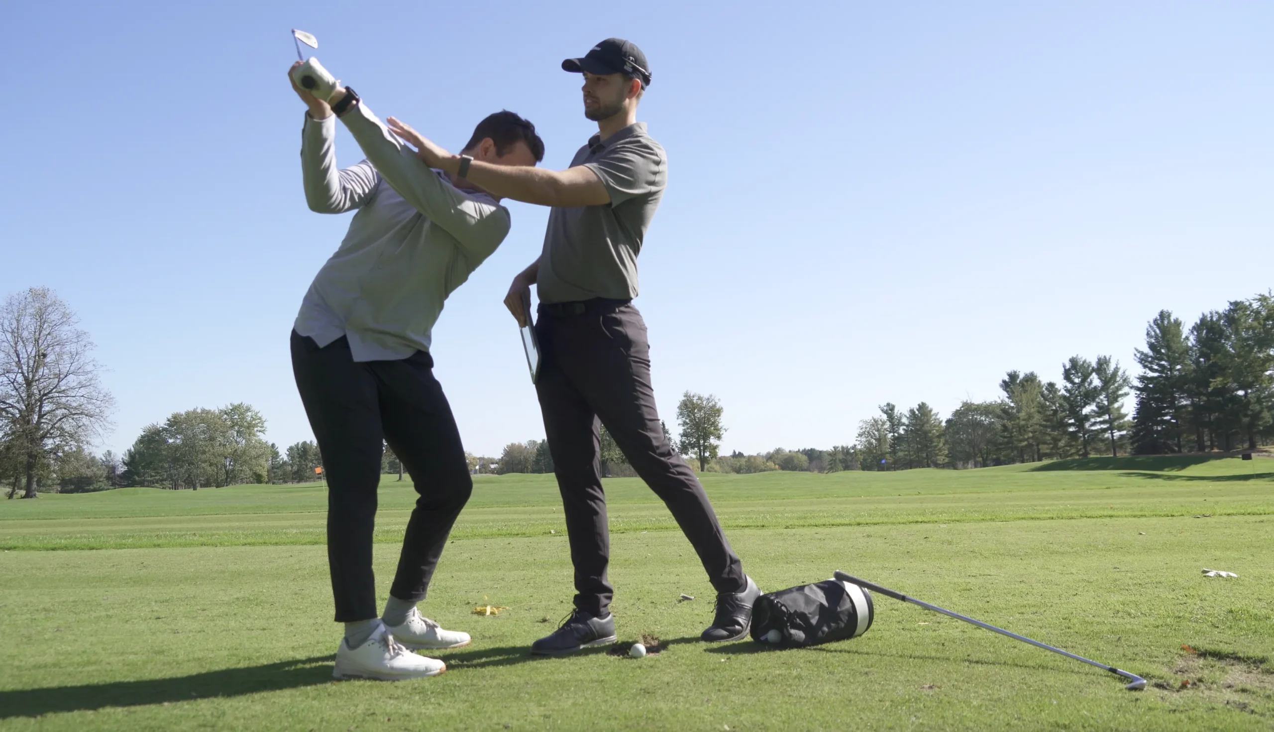 A professional golf instructor adjusting a student's posture during a swing on a sunny outdoor course.