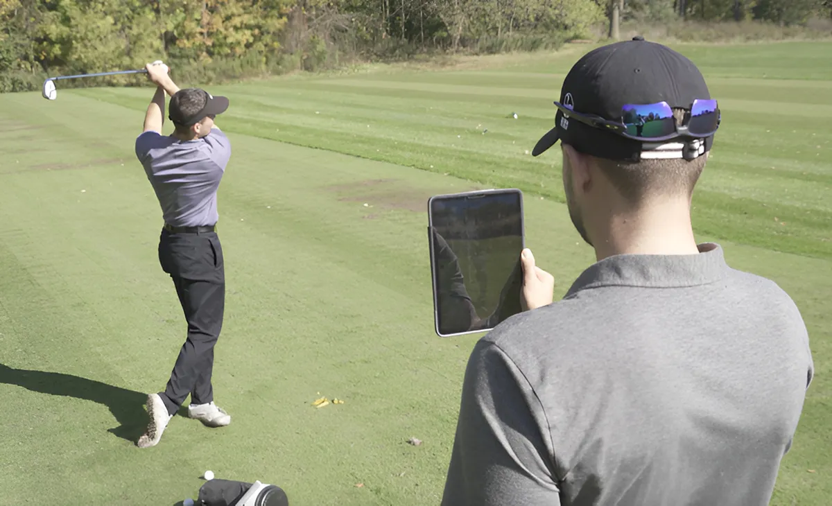 A golf instructor using a tablet to record and analyze a student's swing during an outdoor lesson.