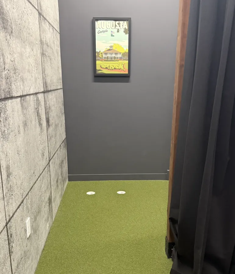 A small indoor golf practice area features a green turf floor with two golf balls